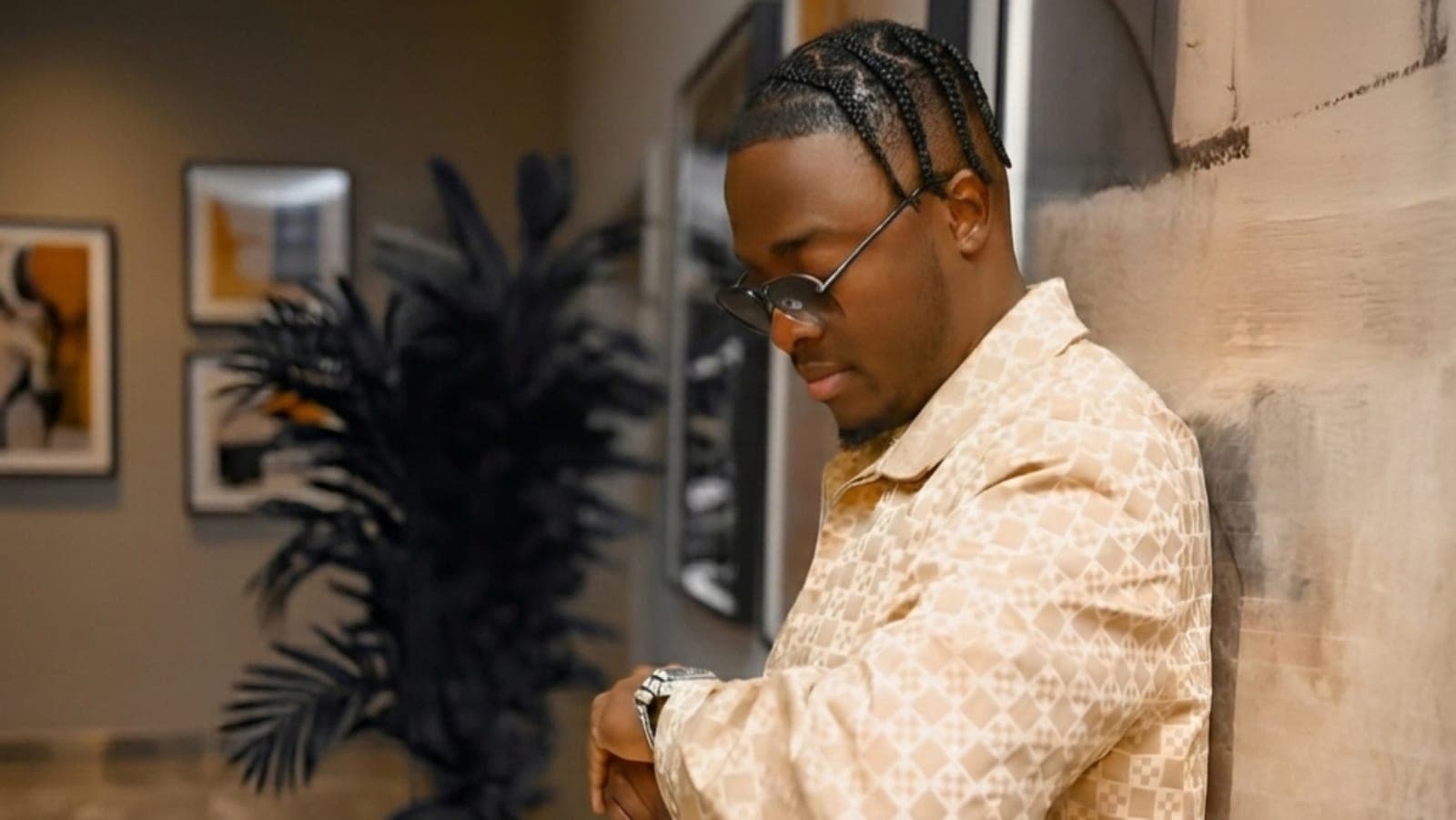 King Kaly in a beige patterned jacket beside a palm