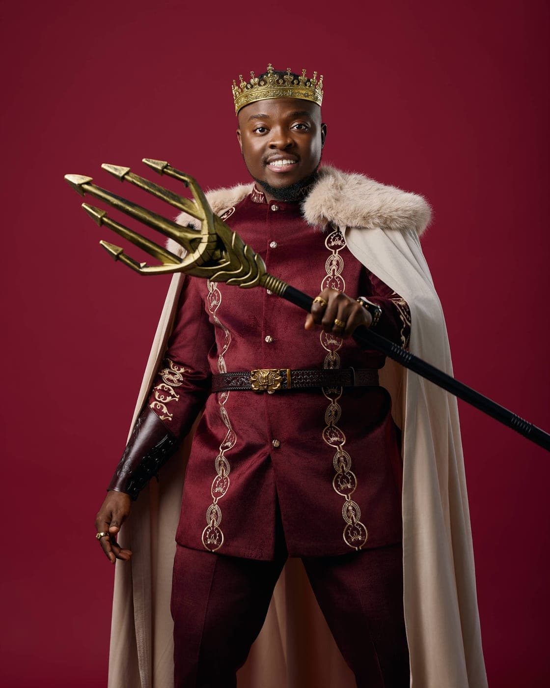 King Kaly in a crown and fur-trimmed cape holding a golden trident