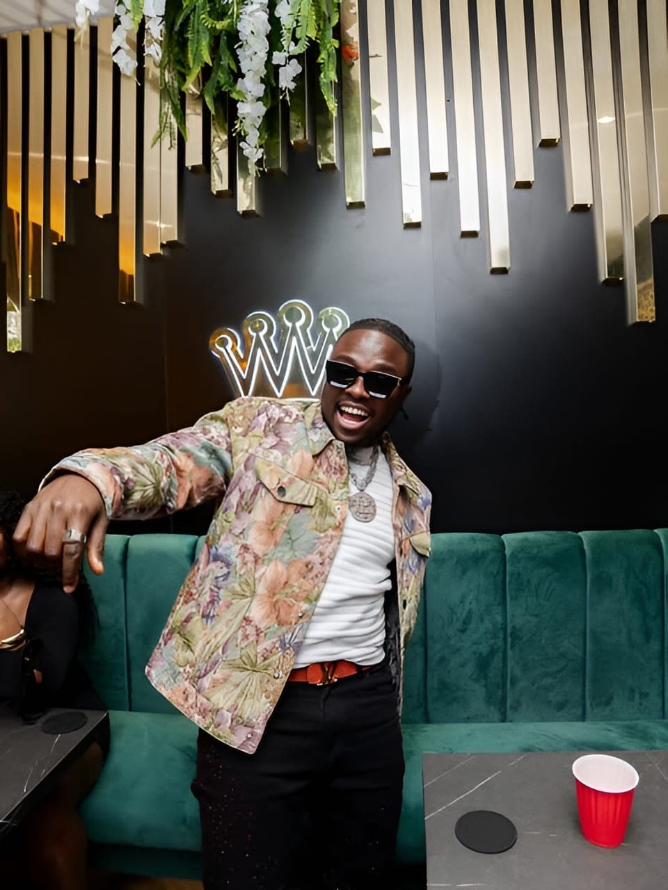 King Kaly in a floral jacket on a green velvet sofa